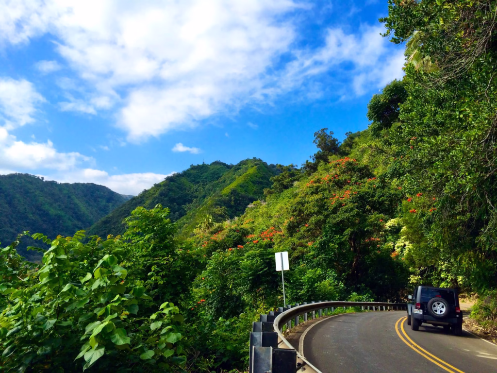 Jeep driving on a curved road with green mountains and blue sky