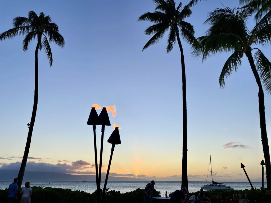 Tiki torches and palm trees along the ocean at sunset in Kaanapali, Maui.