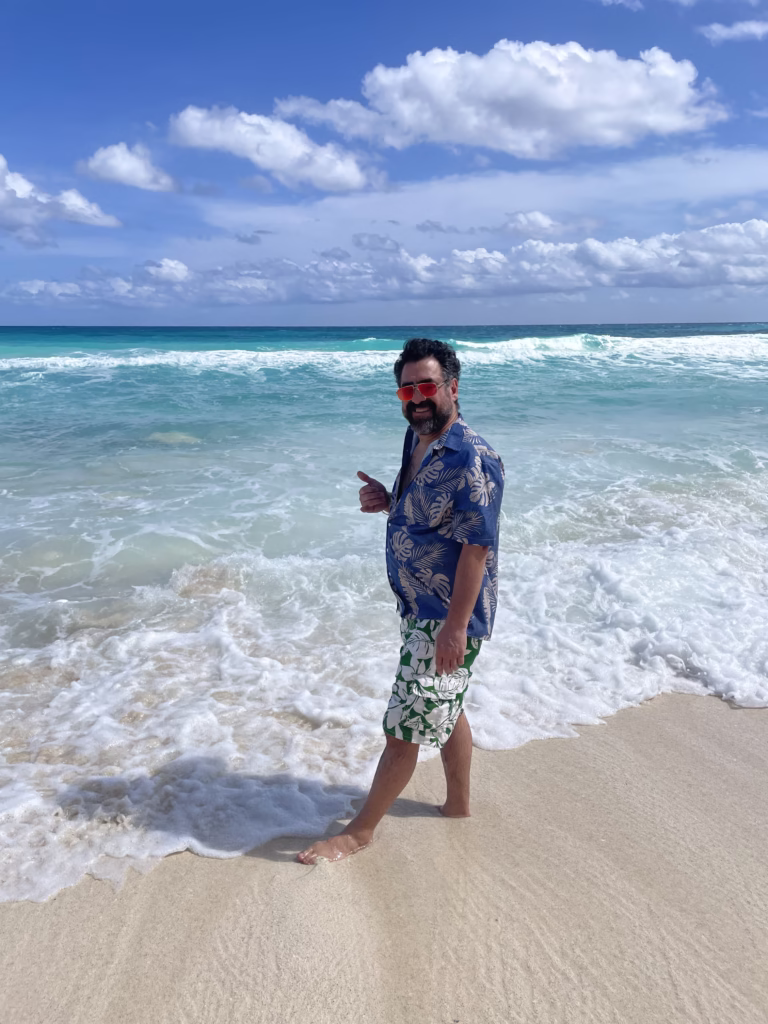 Man giving shaka sign on the beach in Cancun with teal blue ocean behind him.